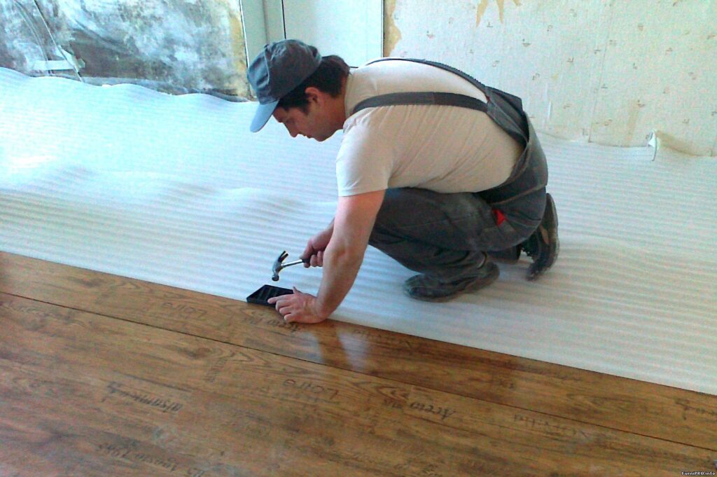A Man in Overall Nailing a Wooden Floor
