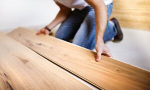 A person is laying down some wood flooring